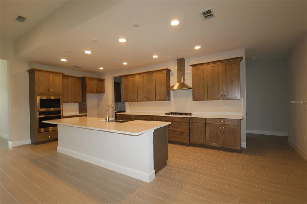 A modern kitchen features wood cabinets, white countertops, a central island, and stainless steel appliances — 3811 WOLVES CREEK PLACE, APOPKA, FL