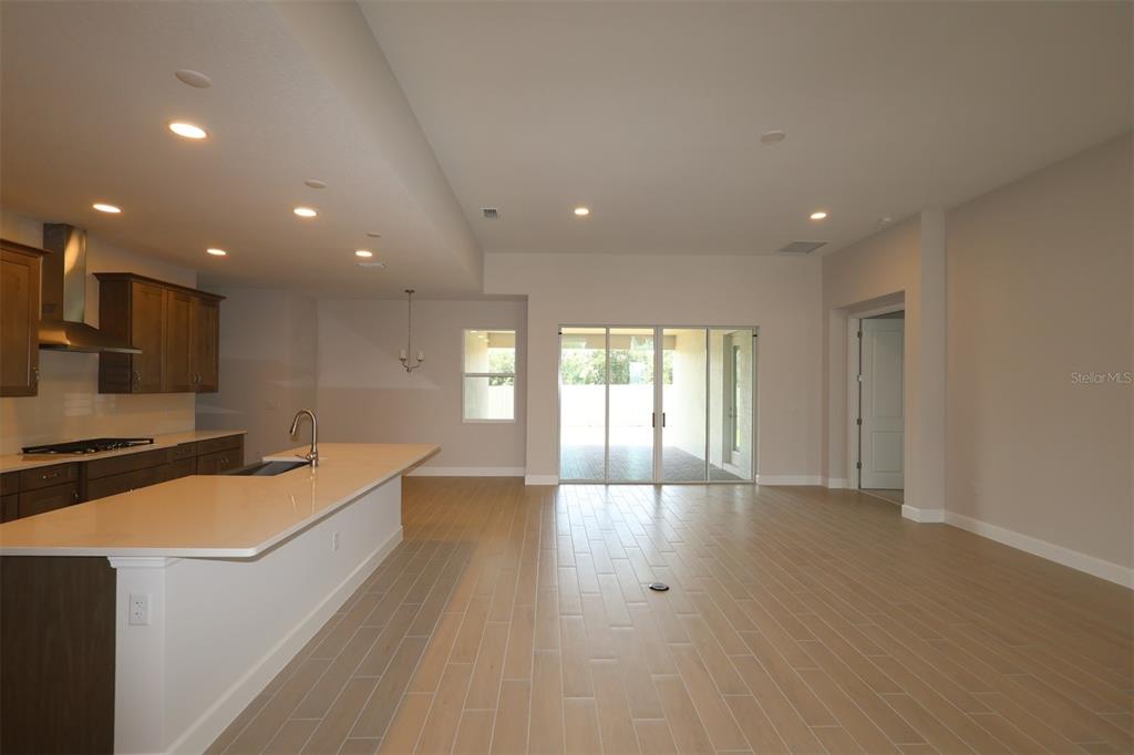 An open-concept room features light wood-look tile flooring, recessed lighting, and a kitchen with cabinets — 3811 WOLVES CREEK PLACE, APOPKA, FL