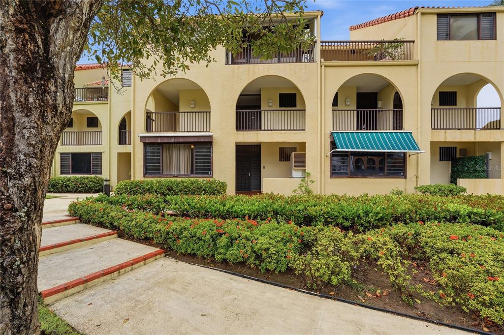 A three-story apartment building with arched balconies, a green awning, and a landscaped front yard — 83 BEACH VILLAGE DR UNIT 83, HUMACAO, PR