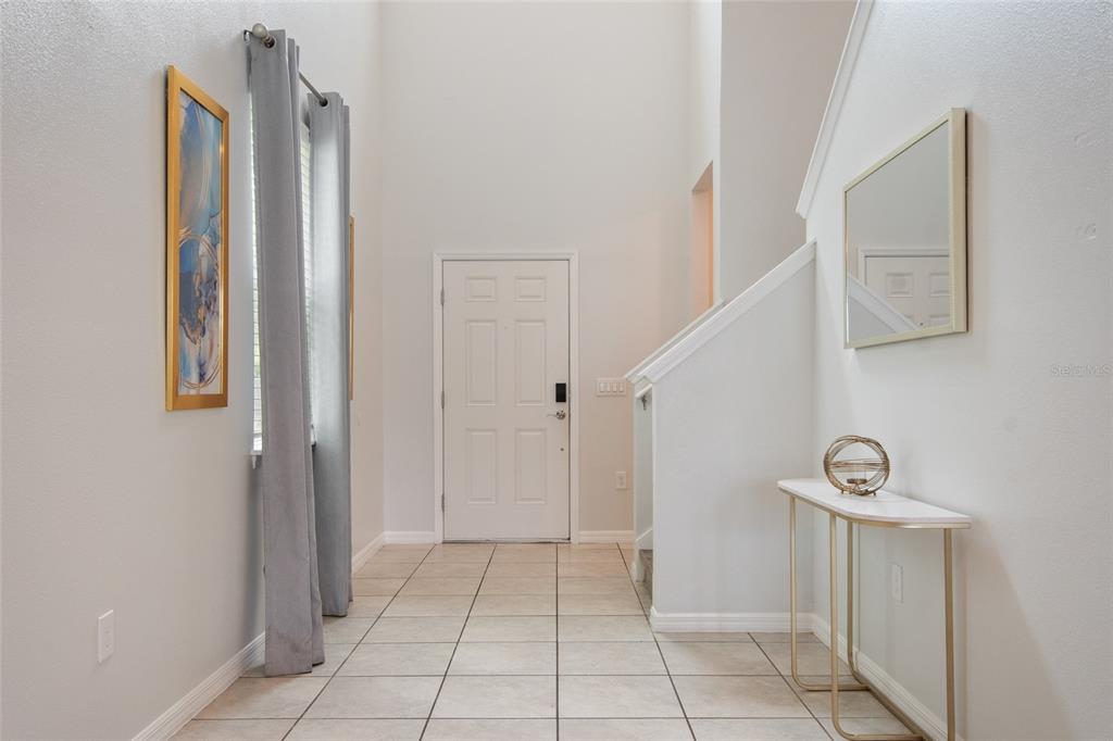 A bright entryway features tiled floors, a white front door, and a staircase with railing — 7364 OAKMOSS LOOP, DAVENPORT, FL