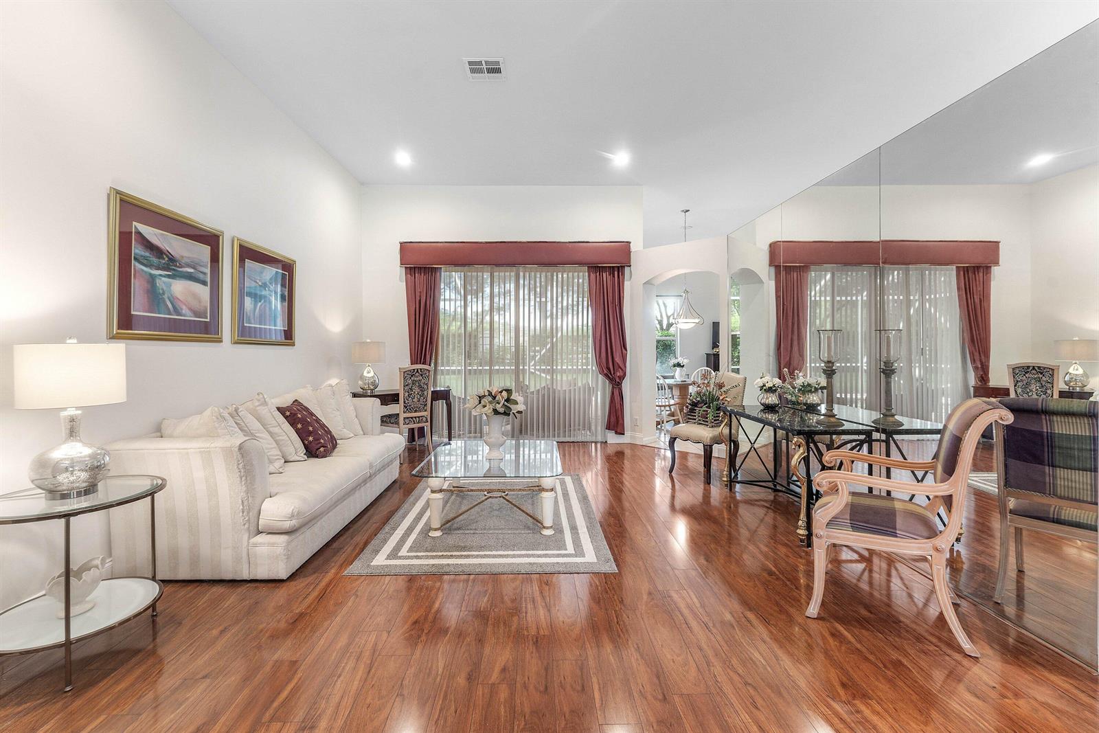 A living room features hardwood floors, a white sofa, a glass coffee table, and mirrors — 4378 Danielson Drive, Lake Worth FL 33467, LAKE WORTH, FL