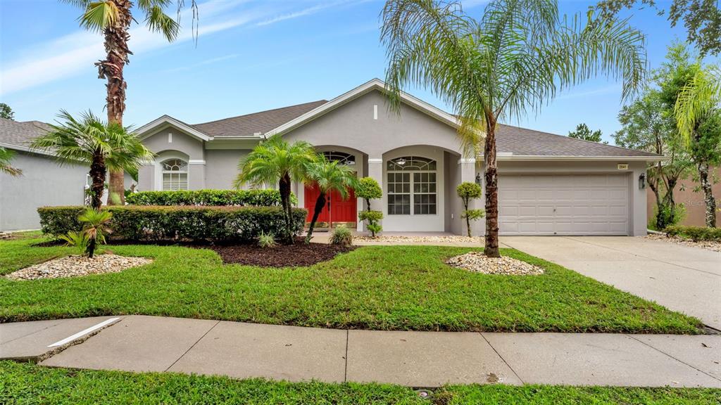 A single-story gray house with a red front door, a two-car garage, and palm trees — 2041 HEARTLAND CIRCLE, VALRICO, FL