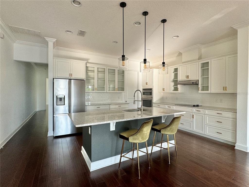 A kitchen features white cabinetry, a dark gray island with two stools, and stainless appliances — 13408 BEEBE ALLEY, ORLANDO, FL