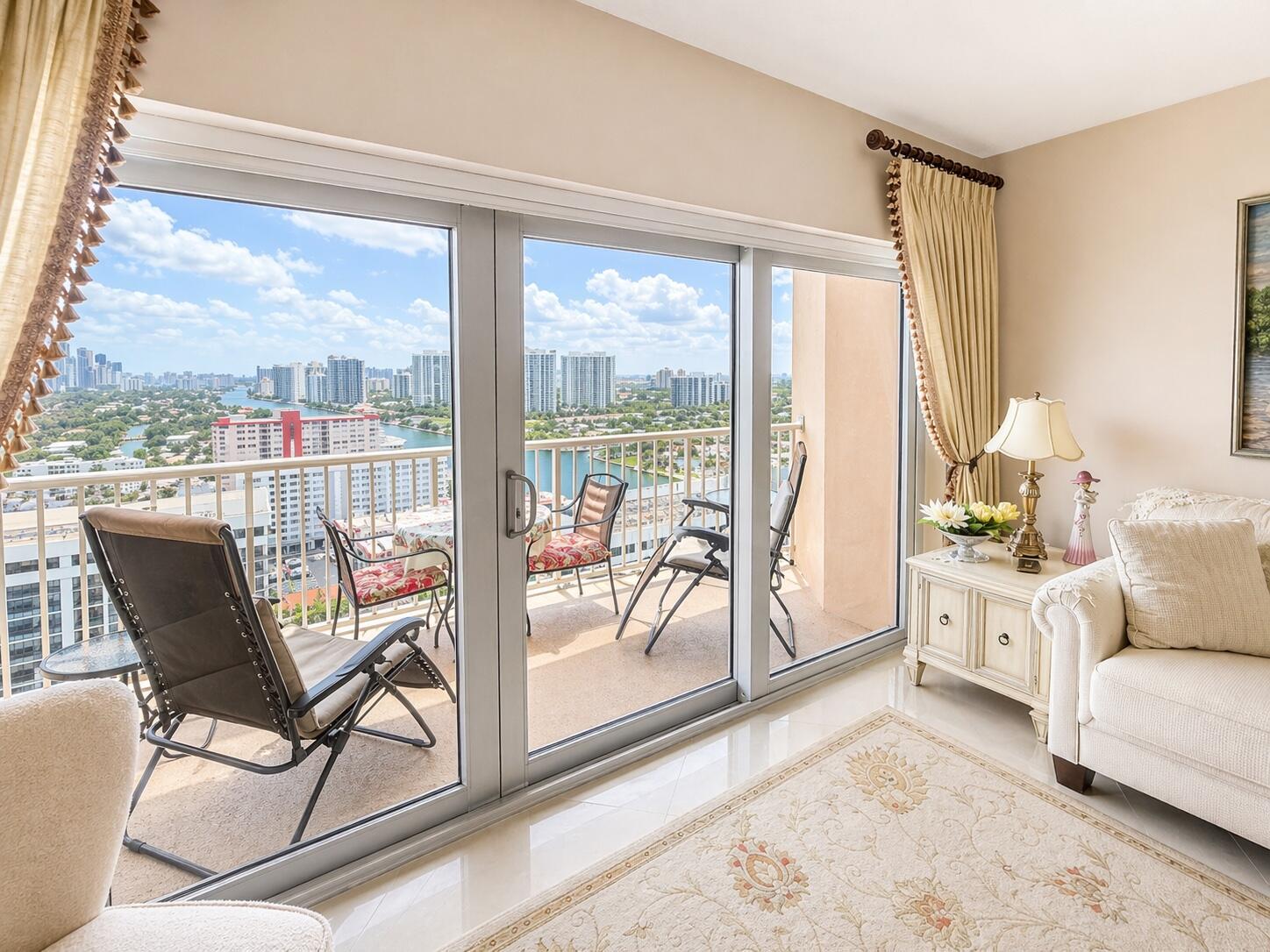 A living room with a beige sofa, area rug, and sliding glass doors opening to a balcony — 1985 S Ocean Drive, Hallandale Beach FL 33009, HALLANDALE BEACH, FL