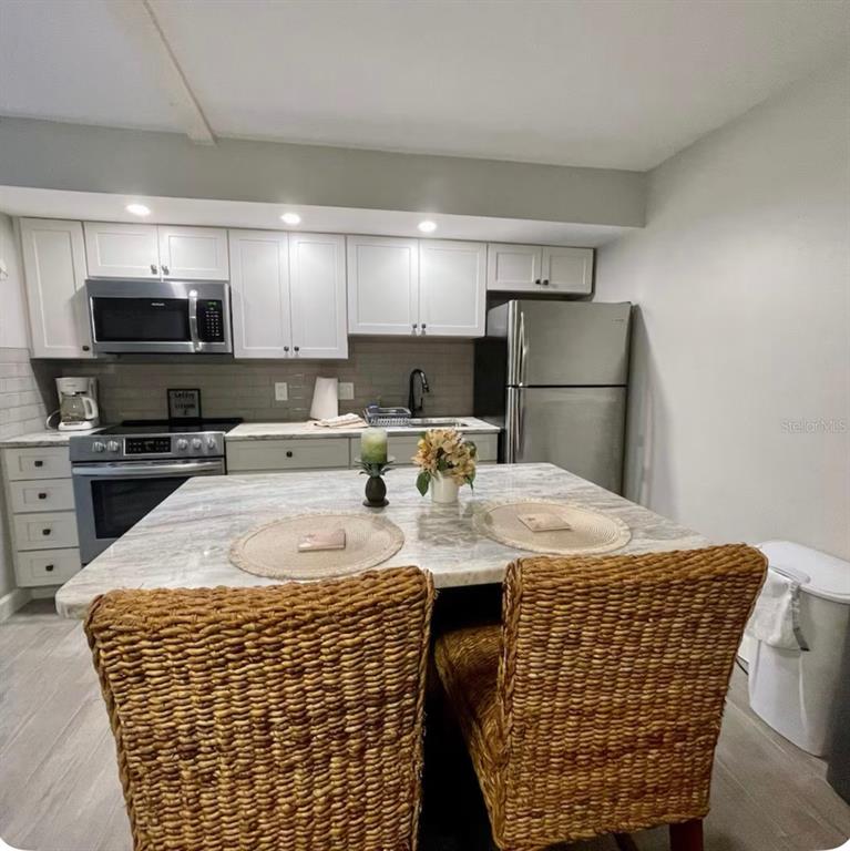 A kitchen features white cabinets, stainless steel appliances, and a central island with wicker chairs — 3700 S ATLANTIC AVENUE UNIT 102, NEW SMYRNA BEACH, FL