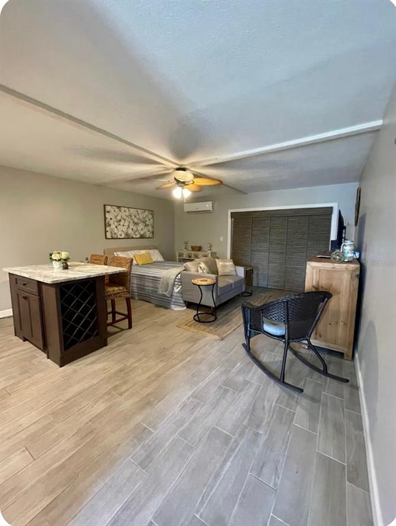 A studio apartment features a kitchen island, a bed, a sofa, and wood-look tile flooring — 3700 S ATLANTIC AVENUE UNIT 102, NEW SMYRNA BEACH, FL
