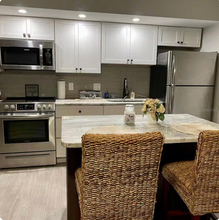 A kitchen with white cabinets, stainless steel appliances, a marble-topped island, and gray tile backsplash — 3700 S ATLANTIC AVENUE UNIT 102, NEW SMYRNA BEACH, FL