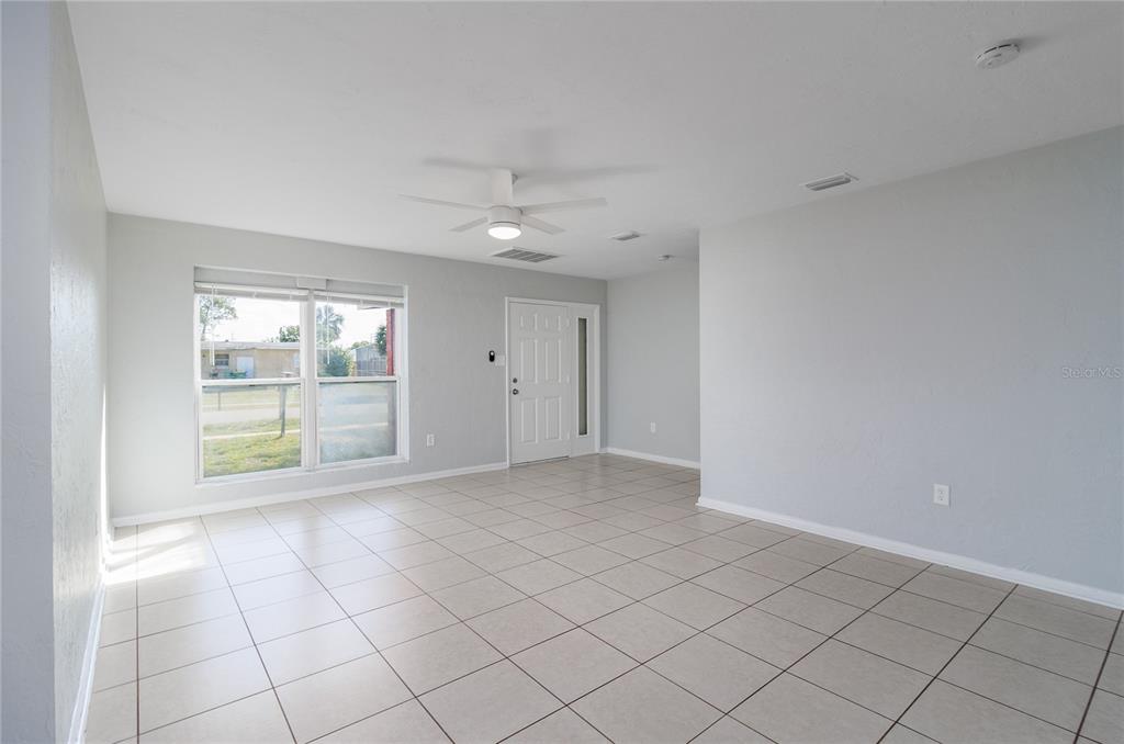 A bright, empty living room features light-colored tile flooring, a ceiling fan, and a front door — 2159 FLOYD COURT, PORT CHARLOTTE, FL
