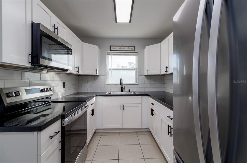 A galley kitchen features white cabinets, black countertops, stainless steel appliances, and a subway tile backsplash — 2159 FLOYD COURT, PORT CHARLOTTE, FL