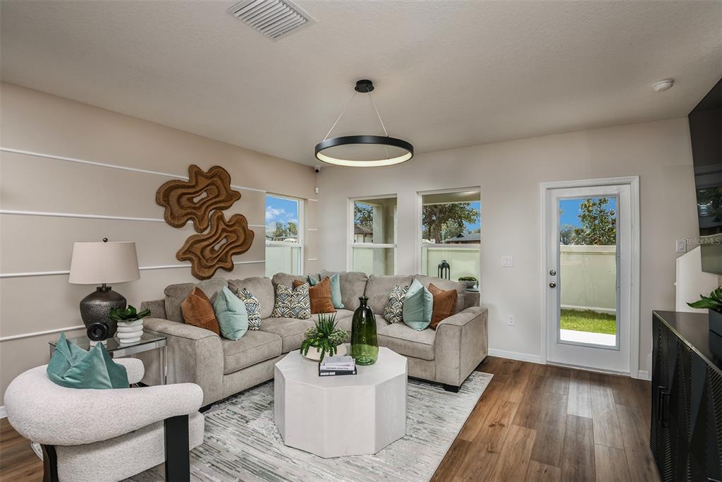 A living room features a sectional sofa, a modern ring chandelier, and wood-look flooring — 4258 HILLOCK BOULEVARD, HAINES CITY, FL