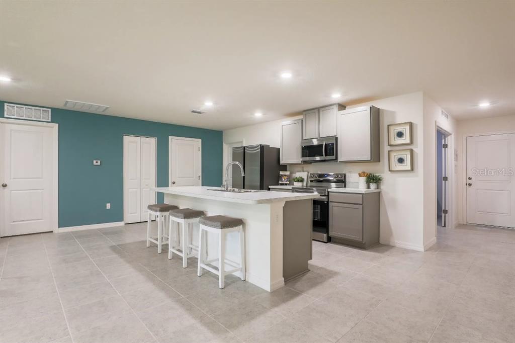 A kitchen features a white island with bar stools, grey cabinetry, and a teal accent wall — 2557 FLAGAMI LANE, NORTH PORT, FL