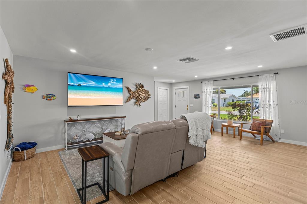 A living room features light wood-look tile flooring, a wall-mounted television, and coastal-themed wall decor — 7307 14TH AVENUE W, BRADENTON, FL