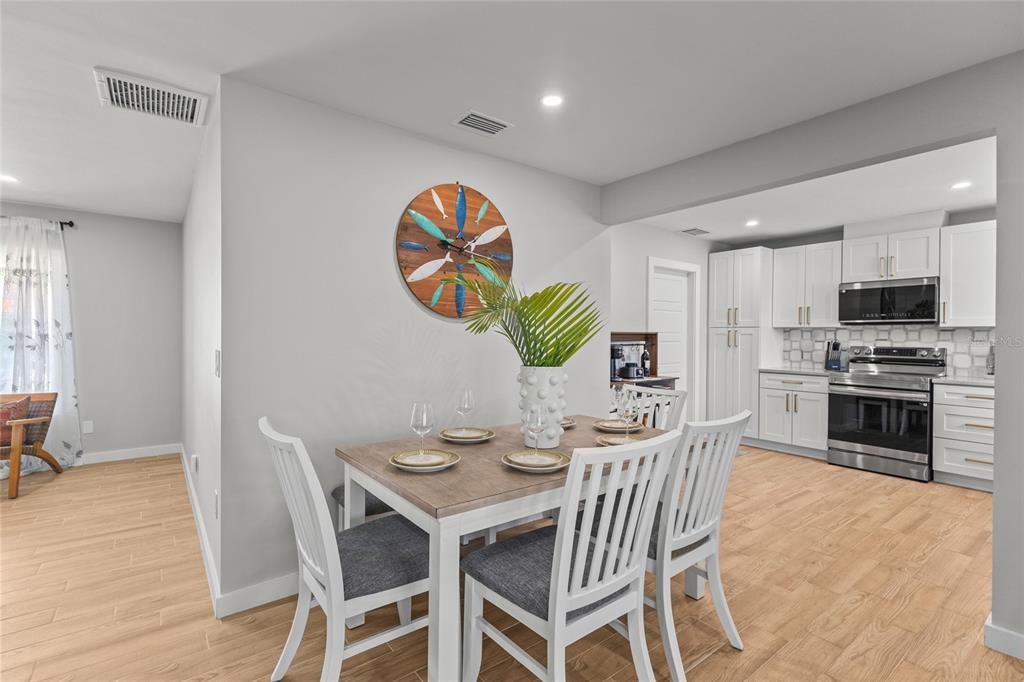 A dining area with a wooden table and white chairs sits adjacent to a white kitchen — 7307 14TH AVENUE W, BRADENTON, FL