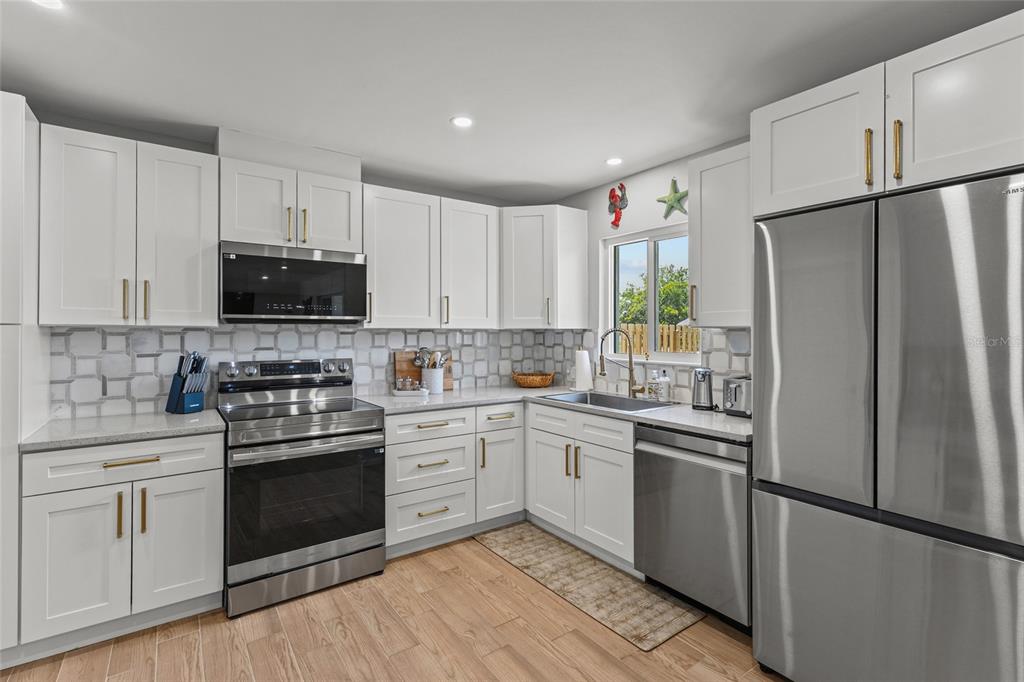 A kitchen features white cabinets, stainless steel appliances, a tiled backsplash, and light wood flooring — 7307 14TH AVENUE W, BRADENTON, FL
