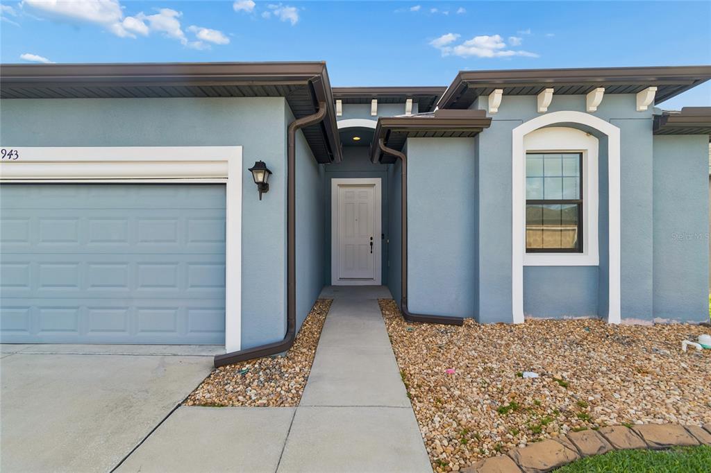 The exterior of a blue house features a white front door, garage, and gravel landscaping — 943 OLD WINDSOR WAY, SPRING HILL, FL