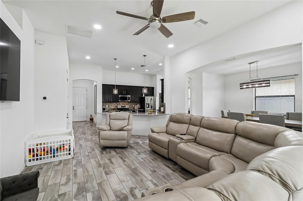 An open-concept living room features light wood-look tile floors, a sectional sofa, and a kitchen — 943 OLD WINDSOR WAY, SPRING HILL, FL