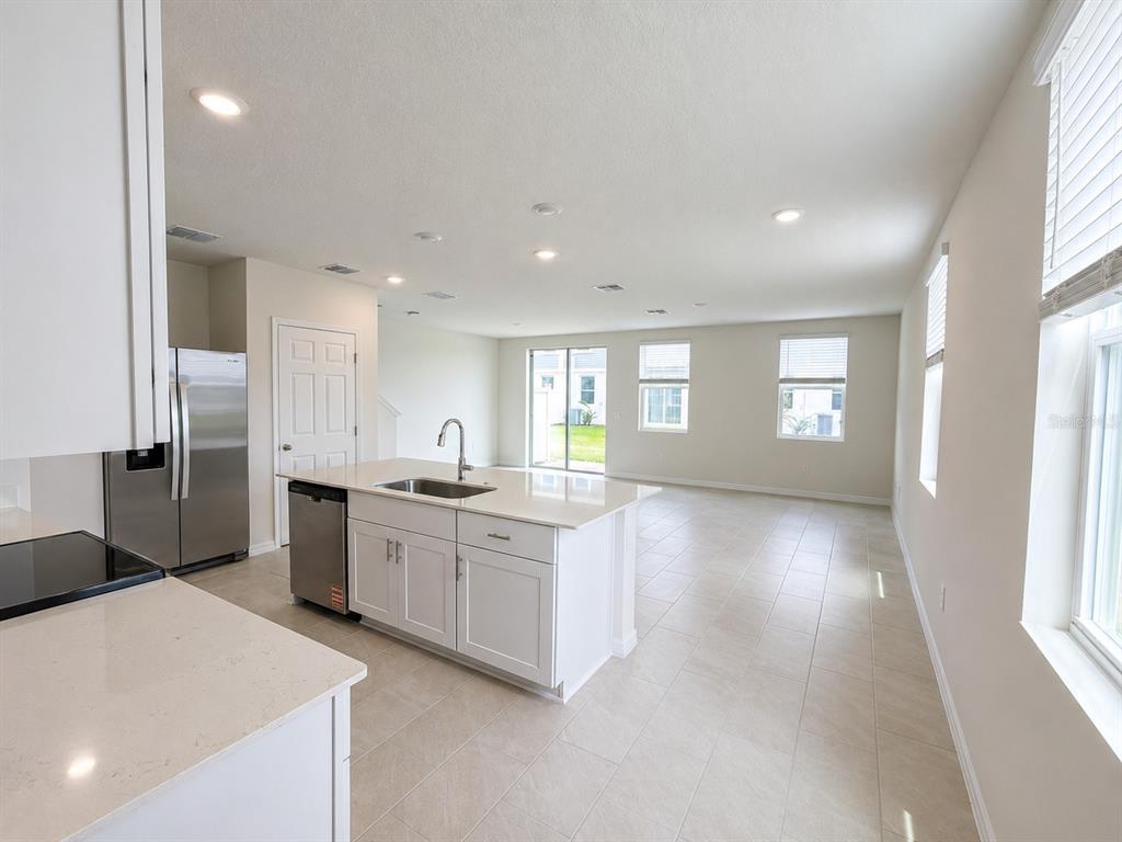A modern kitchen with white cabinets and an island opens into a bright living area — 4595 RANGELAND WAY UNIT 4595, ST CLOUD, FL