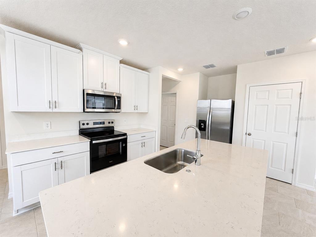 A modern kitchen features white cabinets, stainless steel appliances, and a large quartz-topped island — 4595 RANGELAND WAY UNIT 4595, ST CLOUD, FL