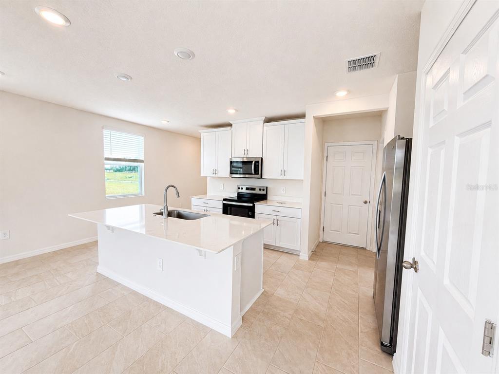 A kitchen features white cabinets, a central island with a sink, and stainless steel appliances — 4595 RANGELAND WAY UNIT 4595, ST CLOUD, FL