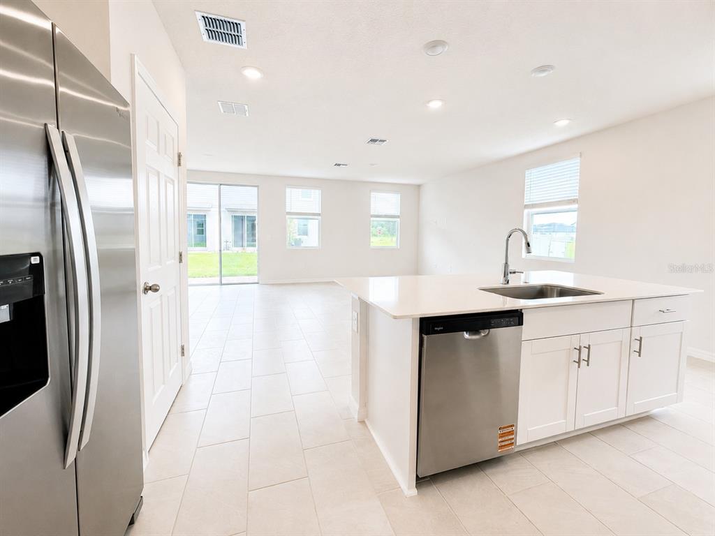 A modern kitchen features white cabinets, a stainless steel dishwasher, and light tile flooring — 4595 RANGELAND WAY UNIT 4595, ST CLOUD, FL