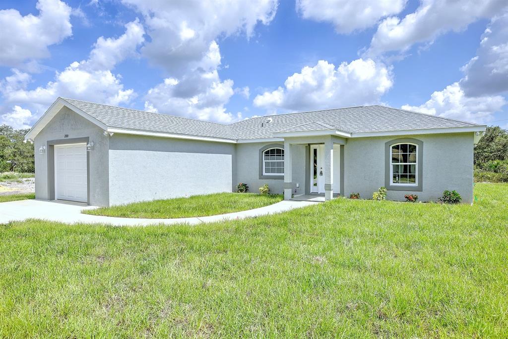 A single-story house with a gray stucco exterior, a white garage door, and a front porch — 2764 W SOMERSET ROAD, AVON PARK, FL
