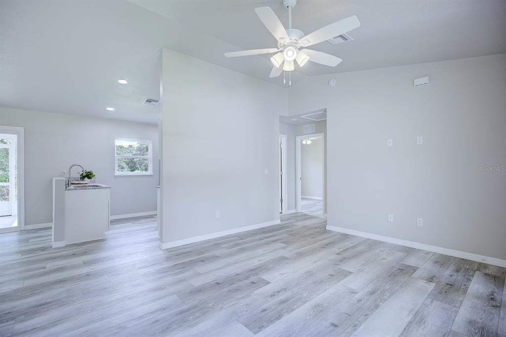 A living room with light gray wood-look flooring, a ceiling fan, and an adjacent kitchen — 2764 W SOMERSET ROAD, AVON PARK, FL