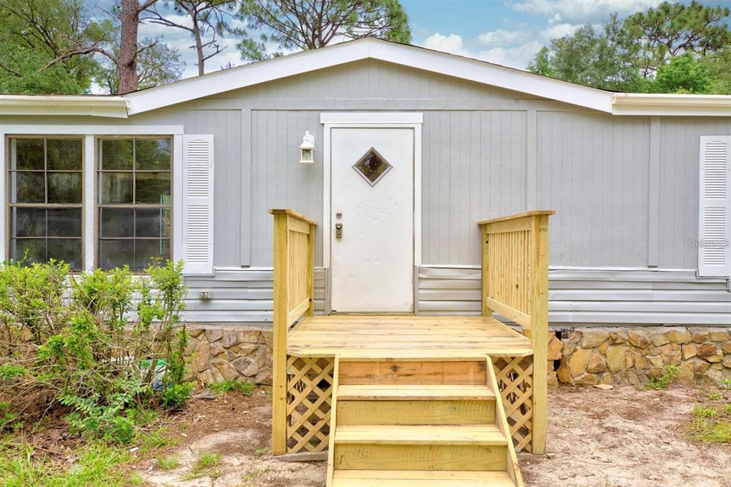 A gray mobile home features a wooden front deck with stairs and stone skirting — 4555 S LEISURE BOULEVARD, LECANTO, FL