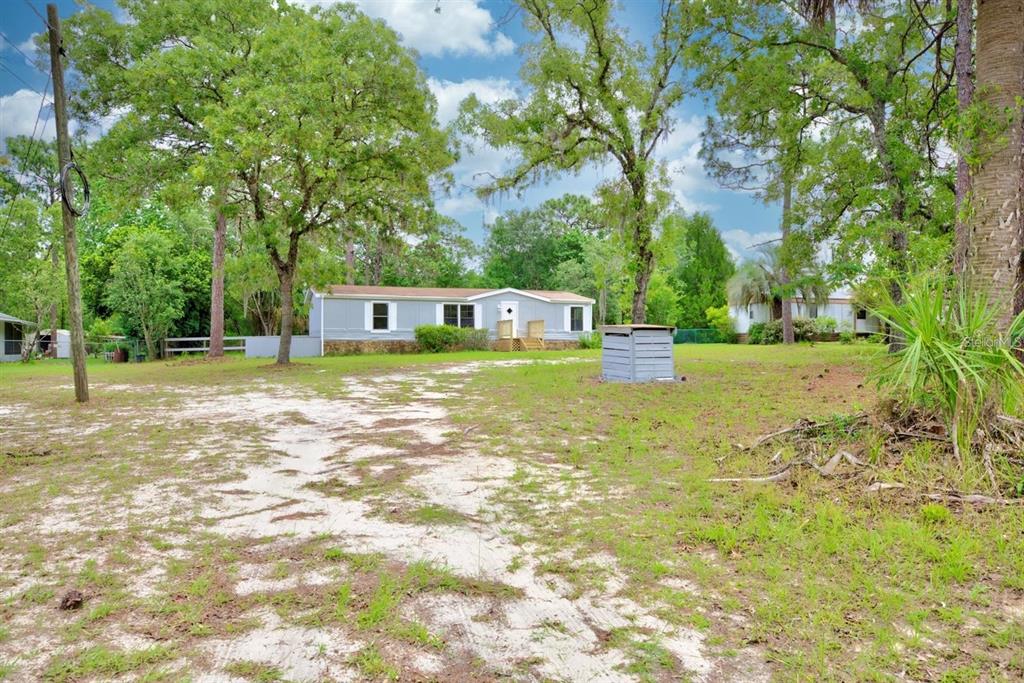A light-colored mobile home sits on a grassy lot with a sandy driveway and trees — 4555 S LEISURE BOULEVARD, LECANTO, FL