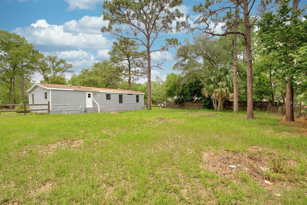 A single-story manufactured home sits on a grassy lot surrounded by tall pine trees — 4555 S LEISURE BOULEVARD, LECANTO, FL