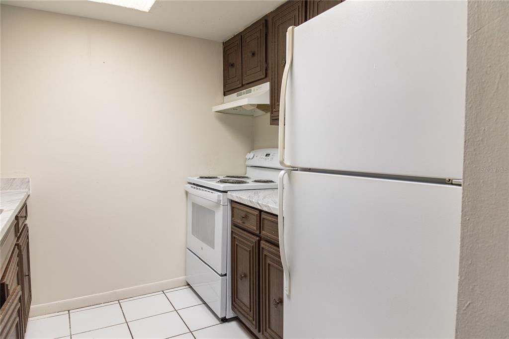 A kitchen features white appliances, dark wood cabinets, and white tile flooring — 4718 JOSEPH COURT UNIT 220, TAMPA, FL
