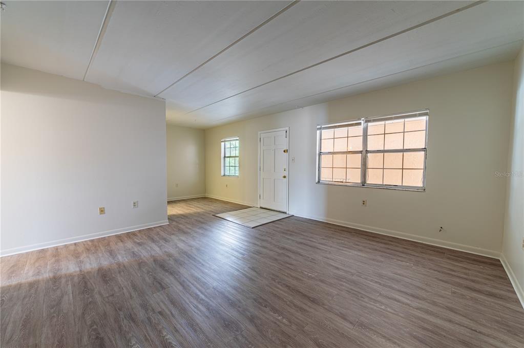 An empty living room features light-colored walls, wood-look flooring, a front door, and two windows — 4718 JOSEPH COURT UNIT 220, TAMPA, FL