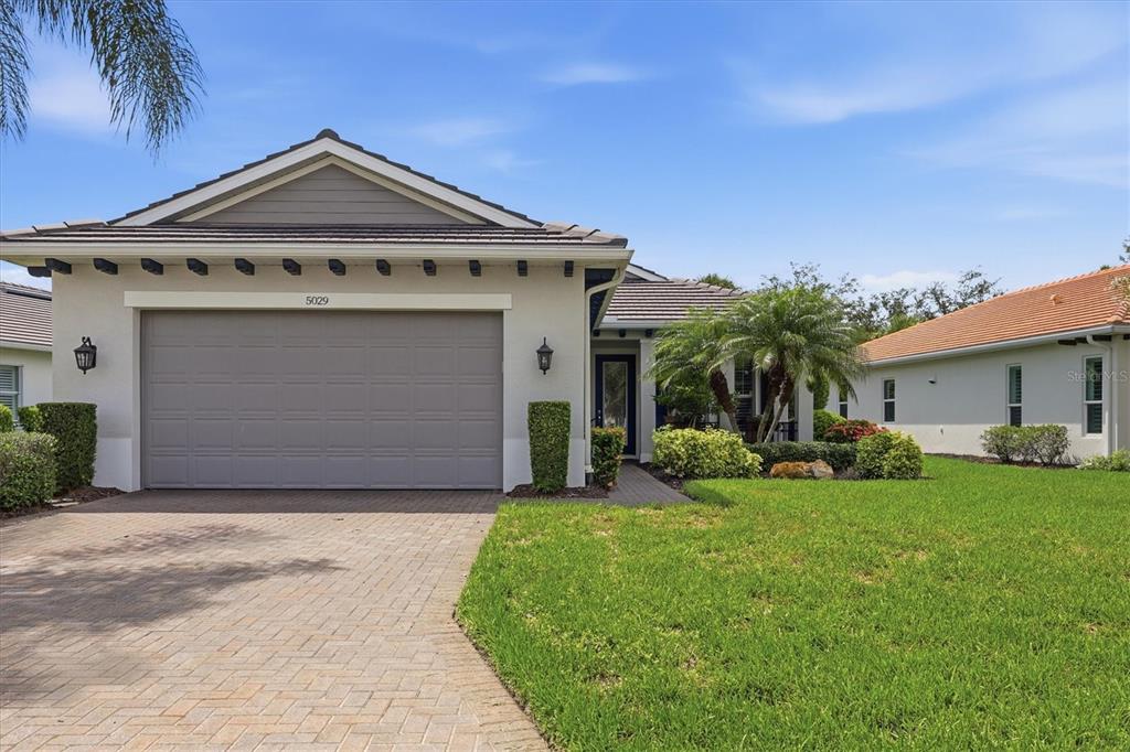 A paved walkway leads to a covered front porch with a blue door and landscaping — 5029 LAKE OVERLOOK AVENUE, BRADENTON, FL