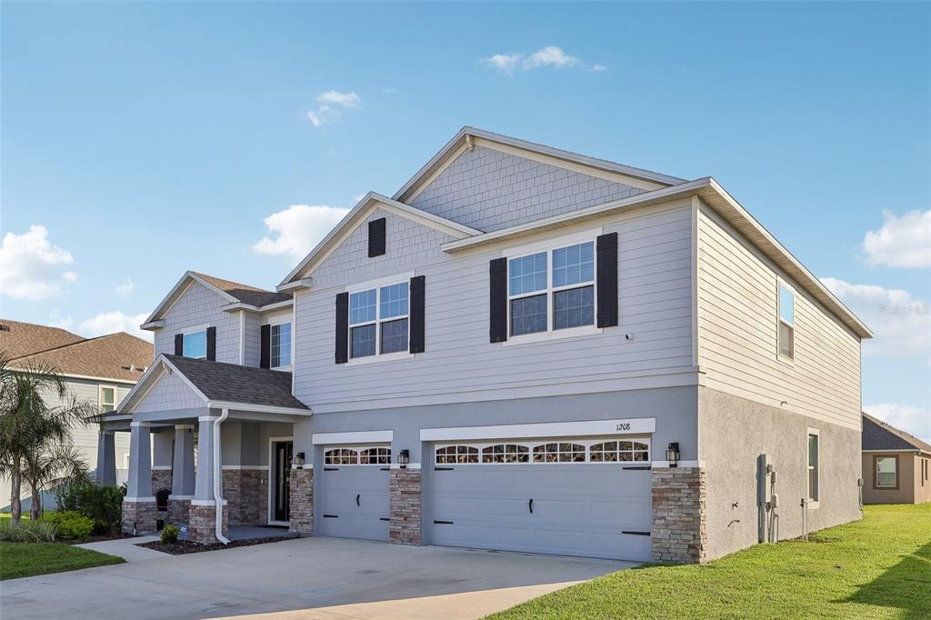 A two-story suburban house with a three-car garage, light gray siding, and stone accents — 1208 HILLBRIDGE DRIVE, HAINES CITY, FL