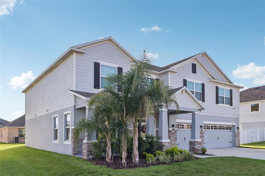 A two-story suburban house with light gray siding, stone accents, and a palm tree out front — 1208 HILLBRIDGE DRIVE, HAINES CITY, FL