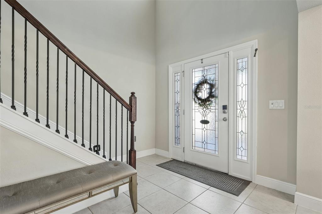 An entryway features a tiled floor, a staircase with iron railings, and a glass-paneled door — 1208 HILLBRIDGE DRIVE, HAINES CITY, FL