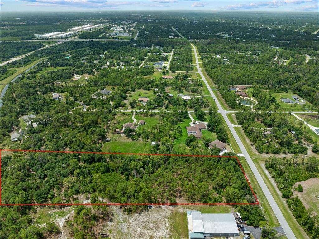 An aerial view shows a rectangular, wooded plot of land outlined in red near a road — N CHAMBERLAIN BOULEVARD, NORTH PORT, FL