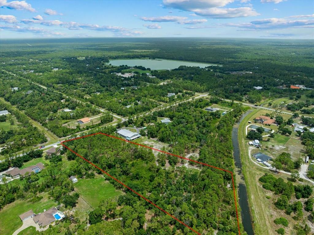 An aerial view shows a wooded, rectangular plot of land outlined in red near a canal — N CHAMBERLAIN BOULEVARD, NORTH PORT, FL