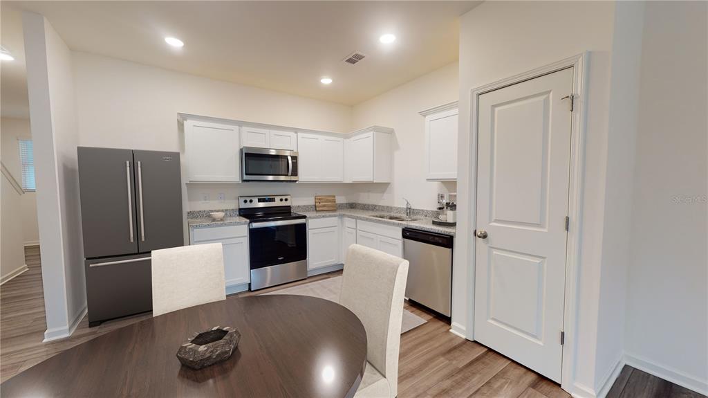 A kitchen with white cabinets, stainless steel appliances, and a dining table in the foreground — 14856 LUCCA WAY, DADE CITY, FL