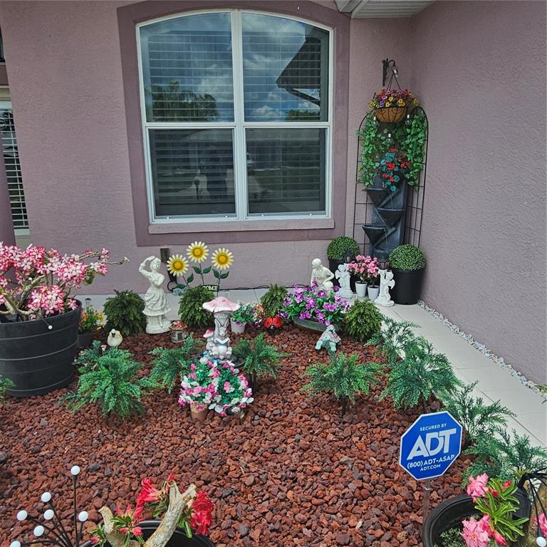 A landscaped garden bed with decorative statues and plants sits below a house window — 8357 DENARGO ROAD, NORTH PORT, FL