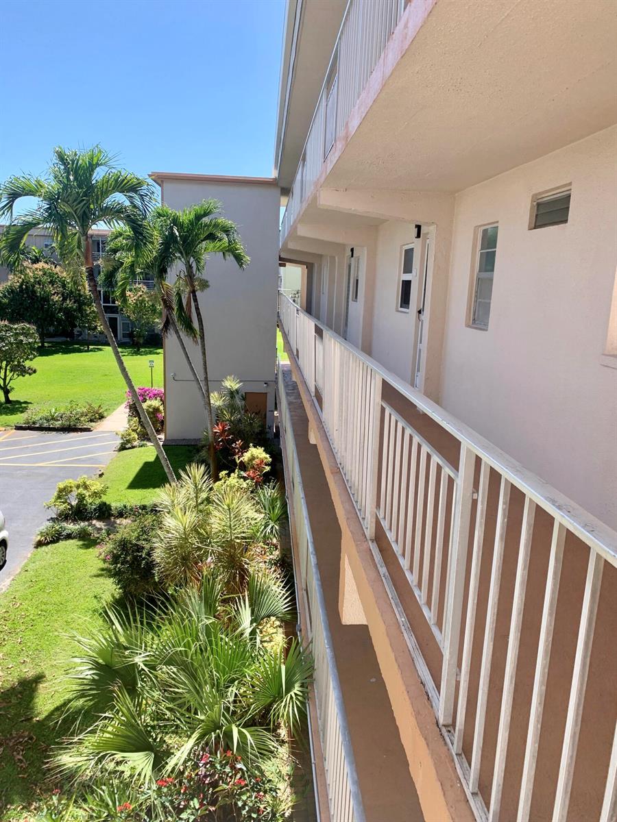 An elevated view of an apartment building exterior walkway overlooking a grassy courtyard and trees — 230 NE 26th Avenue # 318, Boynton Beach FL 33435, BOYNTON BEACH, FL