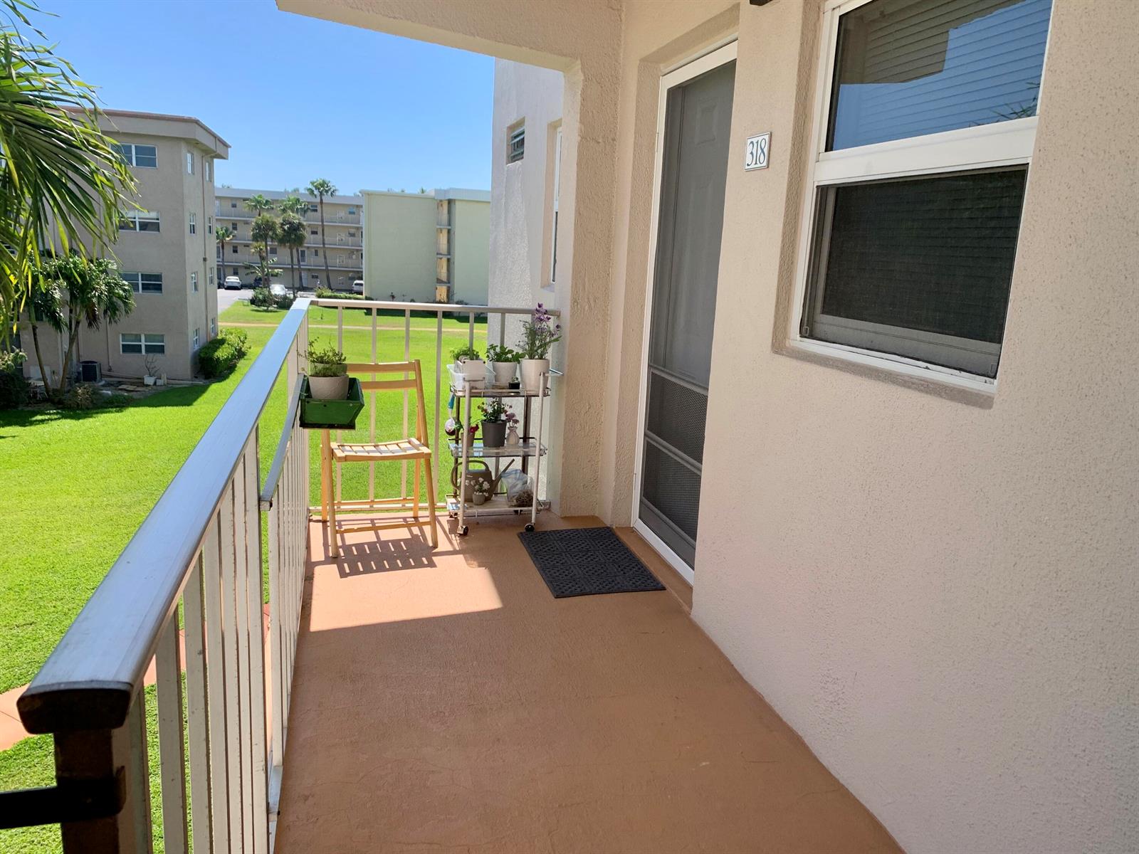 A balcony with a wooden chair, a tiered plant stand, and a view of grass — 230 NE 26th Avenue # 318, Boynton Beach FL 33435, BOYNTON BEACH, FL