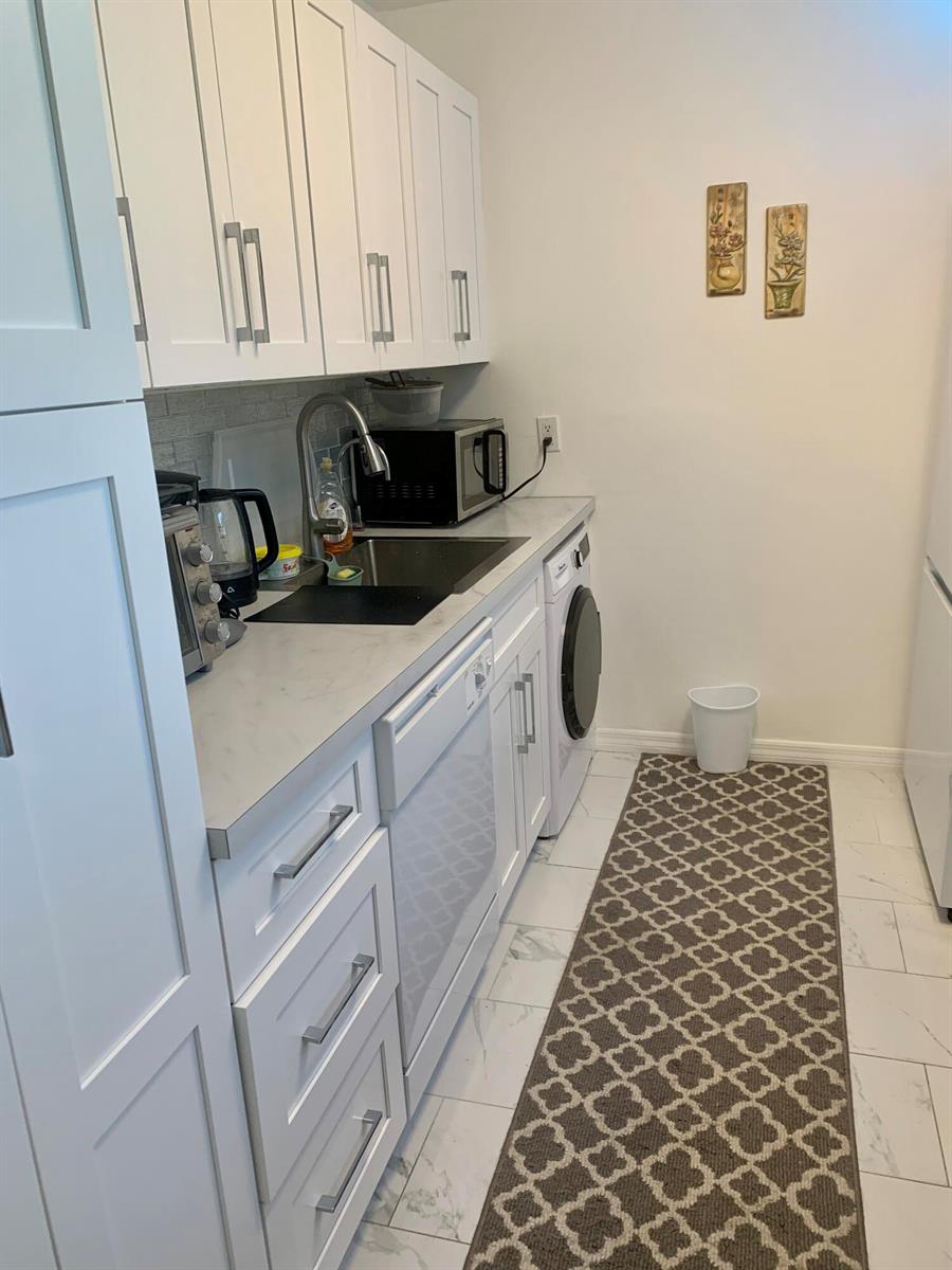 A galley-style kitchen features white cabinets, marble-look countertops, a built-in washer, and tile flooring — 230 NE 26th Avenue # 318, Boynton Beach FL 33435, BOYNTON BEACH, FL