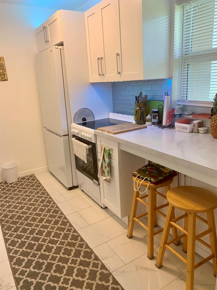 A kitchen features white cabinets, a white refrigerator, a stove, and a breakfast bar — 230 NE 26th Avenue # 318, Boynton Beach FL 33435, BOYNTON BEACH, FL