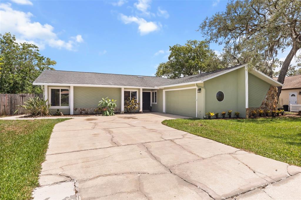 A single-story house with light green siding, a stone base, and a cracked concrete driveway — 12512 WILLOW TREE AVENUE, HUDSON, FL
