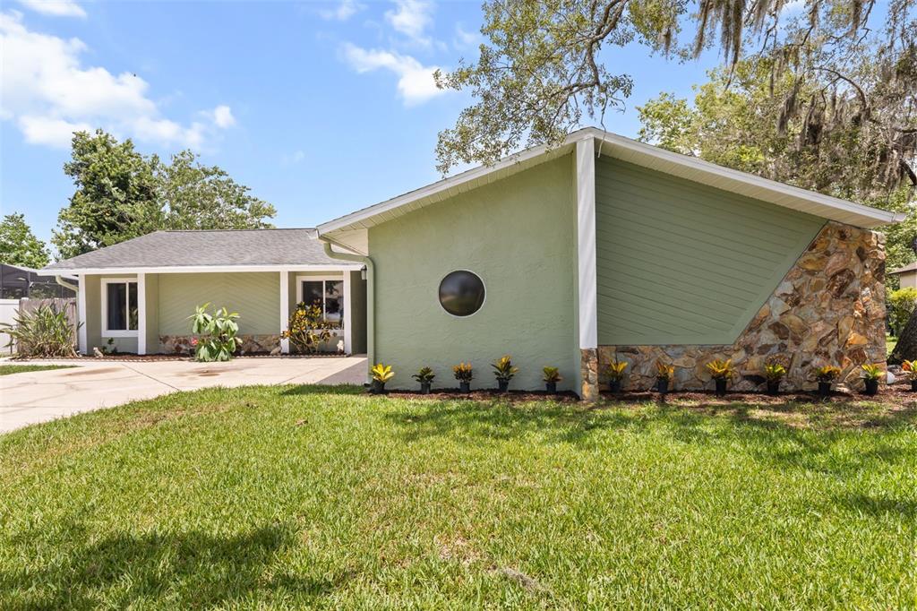 A single-story house with green siding, a stone facade, and a circular window — 12512 WILLOW TREE AVENUE, HUDSON, FL