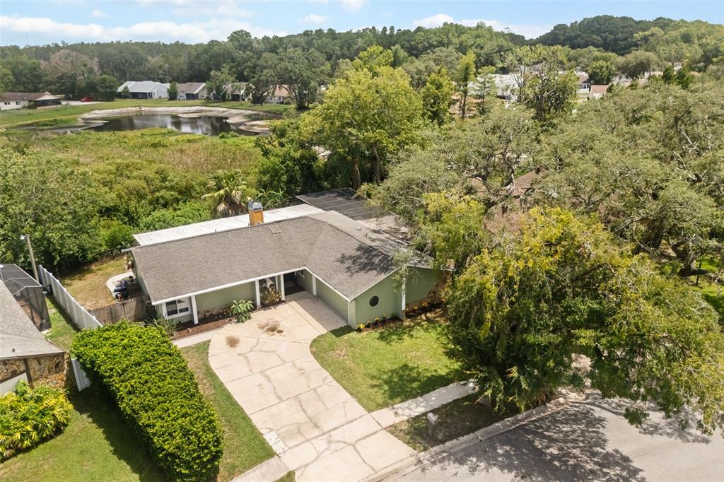 An aerial view shows a single-story house with a driveway, yard, and nearby pond — 12512 WILLOW TREE AVENUE, HUDSON, FL