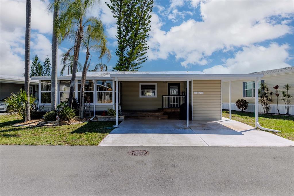 A single-story manufactured home with a carport, tan siding, and palm trees in the yard — 2100 KINGS HIGHWAY CRESCENT UNIT 693, PORT CHARLOTTE, FL