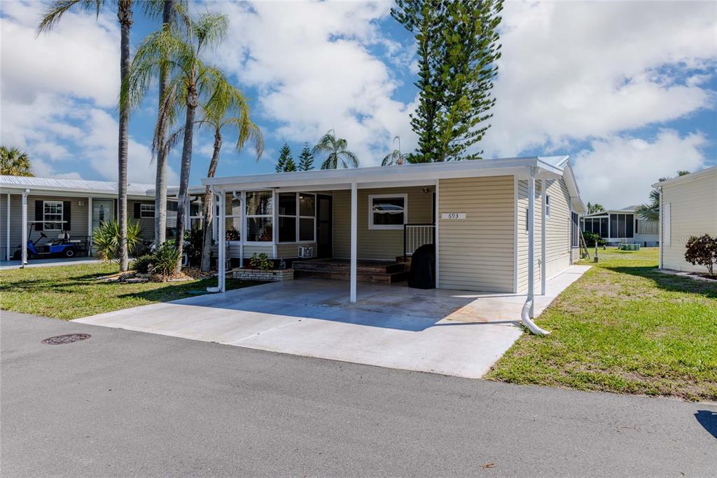 A single-story manufactured home with light yellow siding, a covered carport, and palm trees — 2100 KINGS HIGHWAY CRESCENT UNIT 693, PORT CHARLOTTE, FL