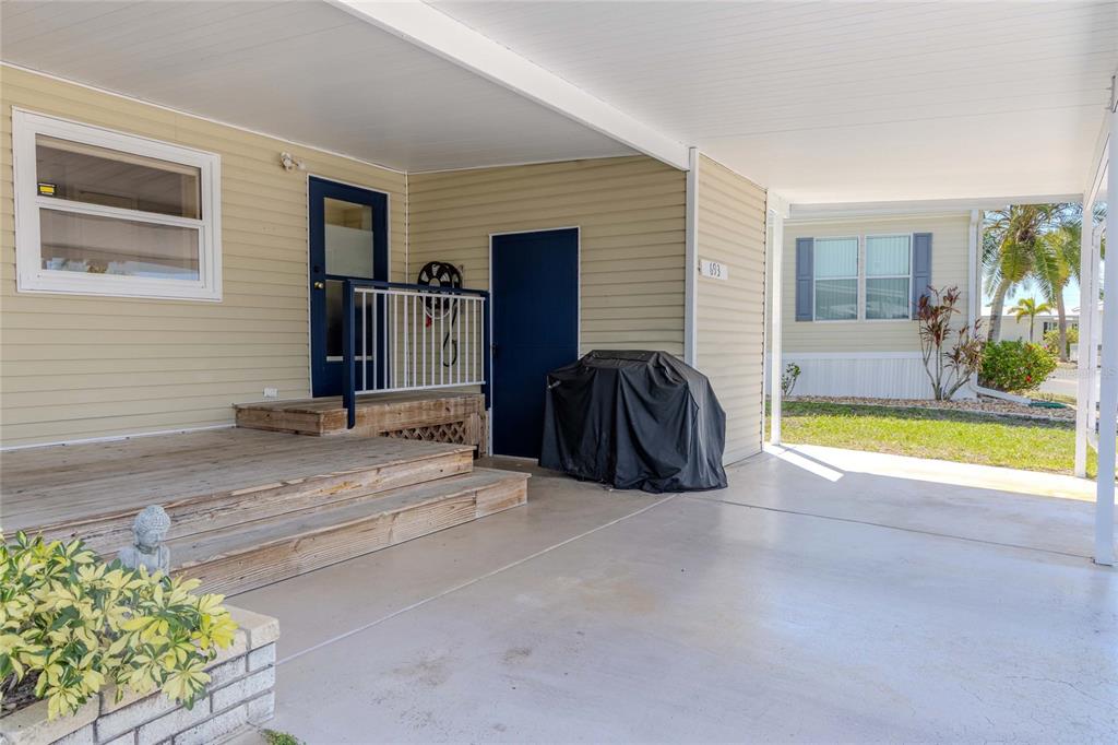 A covered carport leads to a wooden deck and entrance of a light-colored home — 2100 KINGS HIGHWAY CRESCENT UNIT 693, PORT CHARLOTTE, FL