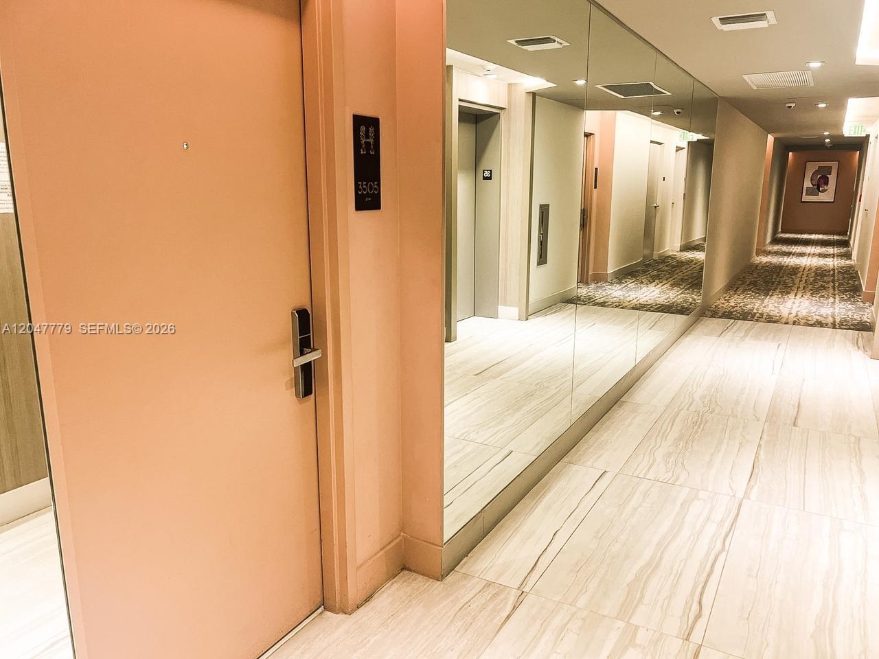 A hallway with a peach-colored door, marble-look flooring, and a large wall mirror — 4010 S Ocean Dr # T3505, Hollywood FL 33019, HOLLYWOOD, FL